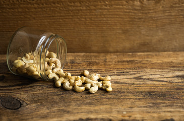 Cashew nuts scattered on the wooden vintage table from a jar. Cashew nut is a healthy vegetarian protein nutritious food.