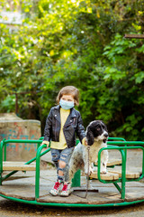 Naklejka na ściany i meble a little cool girl, walking a dog in the Playground, wearing a medical mask, during quarantine, because of the covid-19 pandemic
