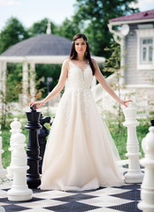 A bride in a wedding dress on a large chessboard. Big chess on the summer playground