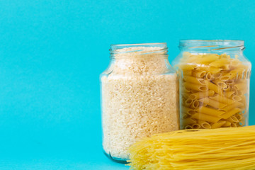 Noodles, rice, pasta in glass jars stand on a blue background. Raw materials for cooking.