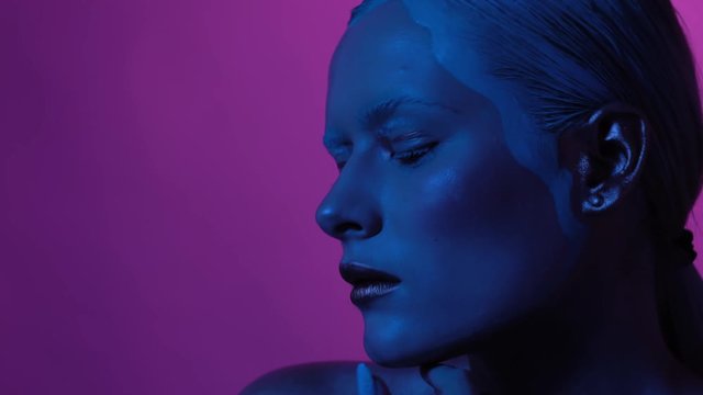 Fashionable look of young woman standing on puple background. Neon lights illuminate all the composition