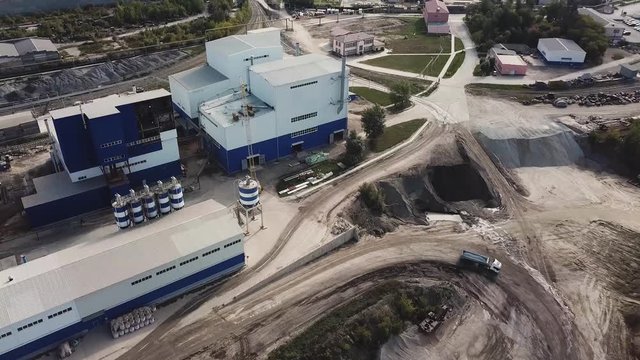 Aerial view of smoke coming out of chimneys of cement production plant in the city area. Stock footage. Ecology concept, industrial enterprise on blue cloudy sky background.