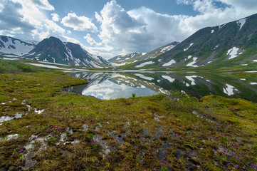 A lake surrounded by mountains with snow and green fields in summer.