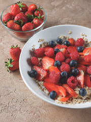 Oatmeal flakes breakfast with fresh berries - strawberry and blueberry  on homemade background and natural morning light.