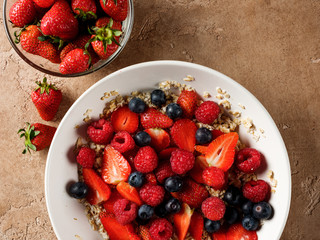 Oatmeal flakes breakfast with fresh berries - strawberry and blueberry  on homemade background and natural morning light.
