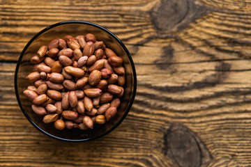 Peanut nuts in a small plate on a vintage wooden table as a background with a copy space.. Peanuts nut is a healthy vegetarian protein nutritious food.