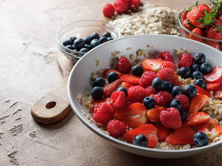 Oatmeal flakes with strawberries and organic berries in white plate with copy space background. Healthy lifestyle concept food.