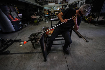 Artist glass blower blowing in his cane the glass paste. A glass crafter is burning and blowing an...