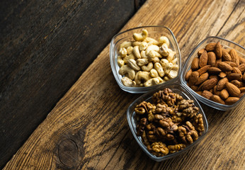Almond, walnut and cashew in a small plates which standing on a wooden vintage table. Nuts is a healthy vegetarian protein and nutritious food. Nuts on rustic old wood.