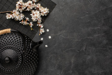 Black teapot with sakura branch on a dark background.Top view with copy space