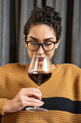 A woman wearing glasses and a sweater smelling red wine