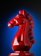 Wooden chess knight in red with blue background © Wes