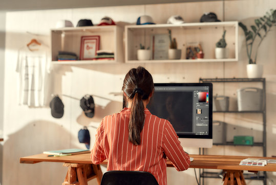 Taking ideas seriously. Portrait of female worker sitting by desk, drawing sketches logo design using pc. Young woman working at custom T-shirt, clothing printing company