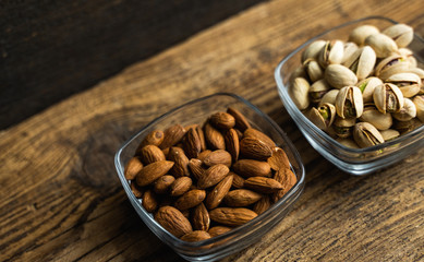 Almond, pistachio in a small plates which standing on a wooden vintage table. Nuts is a healthy...