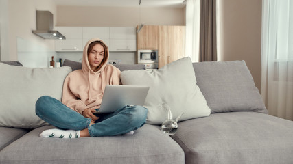Fototapeta premium Too much relaxed. Young caucasian woman sitting on the couch at home, trying to use laptop after smoking marijuana from a bong or glass water pipe