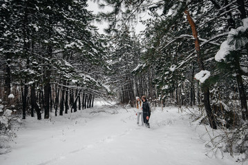 A couple embraces in a snowy forest against a background of trees