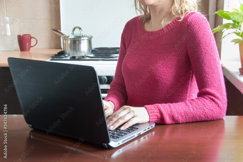 Wall mural Woman sitting at the kitchen with laptop surfing the net, working or studying. Work from home concept. Remote studying