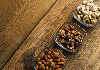 Fototapeta na wymiar Almond, pistachio and walnut in a small plates which standing on a wooden vintage table. Nuts is a healthy vegetarian protein and nutritious food. Nuts on rustic old wood.