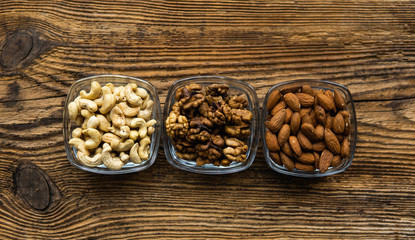 Almond, walnut and cashew in a small plates which standing on a wooden vintage table. Nuts is a healthy vegetarian protein and nutritious food. Nuts on rustic old wood.