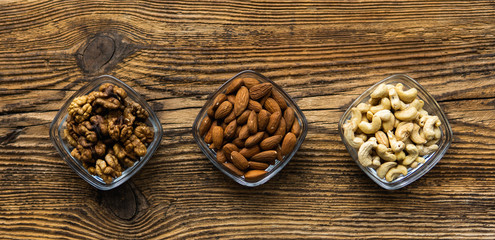 Almond, walnut and cashew in a small plates which standing on a wooden vintage table. Nuts is a healthy vegetarian protein and nutritious food. Nuts on rustic old wood.