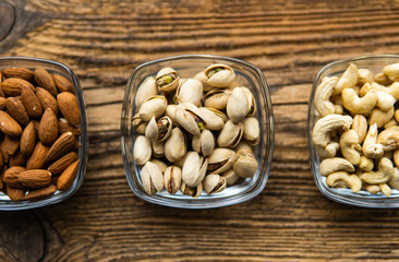 Almond, pistachio and cashew in a small plates which standing on a wooden vintage table. Nuts is a healthy vegetarian protein and nutritious food. Nuts on rustic old wood.