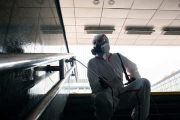 Coronavirus pandemic. disinfection worker in a protective suit and respirator handles handrails with a spray on the street, sanitary work in the city