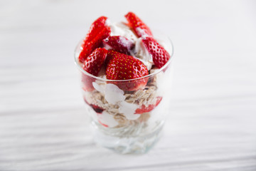 Strawberry dessert in a plate with ice cream and cream on a white wooden background