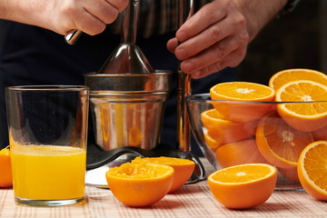 Squeezing an orange with a manual press, close view, making a glass of fresh. Fresh oranges on a wooden table, whole, squeezed and sliced.