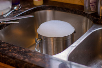 stainless steel bucket filled with soapy bubbles in sink
