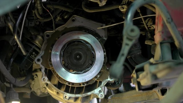 Mechanic is uninstalling a car clutch. Car service worler with diry hands taking off car clutch close up.