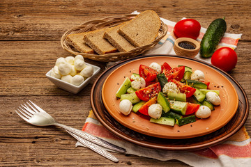 Fresh salad from tomato, cucumber and baby mozzarella. Sunny lunch with crusty bread