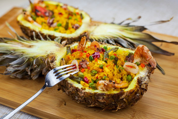 two pineapple halves with rice and seafood on wooden background, view from the top