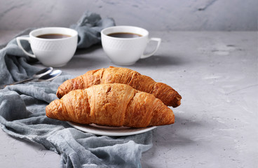Two fresh croissants and two cups of coffee on a light grey concrete background. Breakfast or lunch concept. Copy space