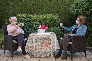 Senior woman and daughter with face masks having coffee at social disctance 