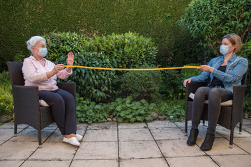 Senior woman and daughter with face masks measuring safety distance 