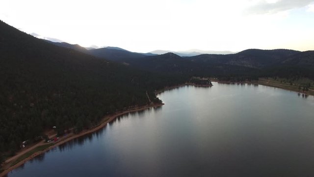 Aerial view of calm lake by forest against sky during sunset, drone moving slowly over beautiful water body by mountains - Lake Wellington, Colorado