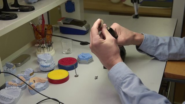 Close-up of a dental technician holding a dental drill in his hands and working on creating dentures in a laboratory