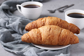 Two fresh croissants and two cups of coffee on a light grey concrete background. Breakfast or lunch concept. Horizontal format