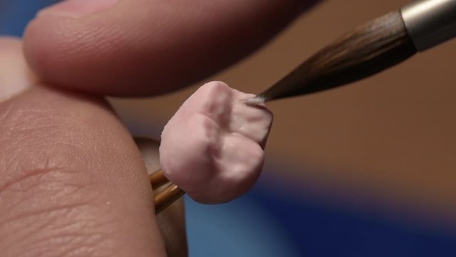 Dental technician applies ceramic material to the crown of a dental implant in a dental laboratory using tweezers and a brush. Dental technology close-up.