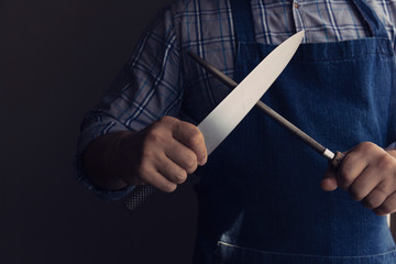 male chef hands sharpening knife with sharpening rod. Dark background. Low key