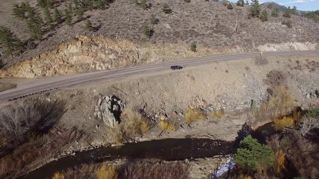 Aerial view of van on roadside by river during sunny day, drone moving forward towards vehicle on highway - Red Rocks, Colorado