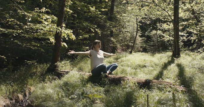 Woman practice yoga meditation sitting on a tree trunk on a forest clearing in nature on a post coronavirus reopening staycation at the end of pandemic