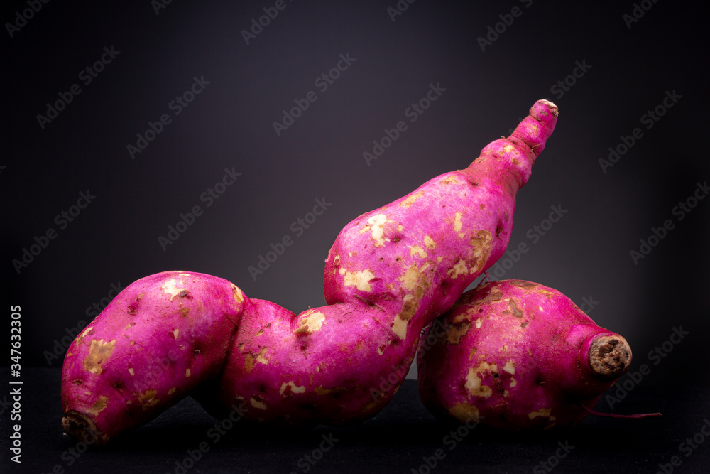 Wall mural couple of shiny magenta fresh vibrant colourful organic raw sweet potato or yam in studio lighting c