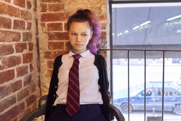 Portrait of 15 years old teenage girl in school uniform with tie sitting on chair