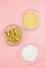 Dried chamomile, yellow clay and sea salt in a glass bowl on a pink pastel background . The concept of creating natural cosmetics and home personal care
