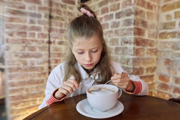 Girl child 9, 10 years old with cup of hot chocolate sitting in cafe at table