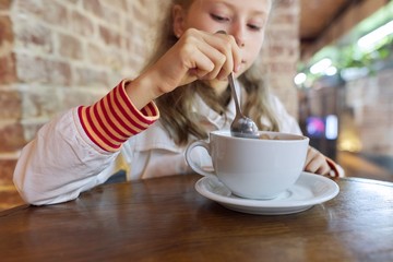 Girl child 9, 10 years old with cup of hot chocolate sitting in cafe at table