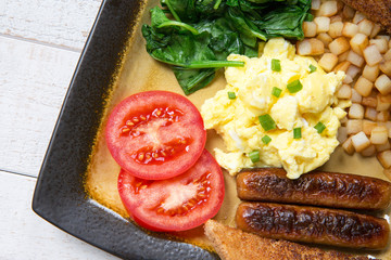 country style breakfast plate of scrambled eggs and sausage with sides of hash browned potato,...