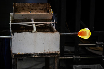 Glass blower forming beautiful piece of glass. A glass crafter is burning and blowing an art piece