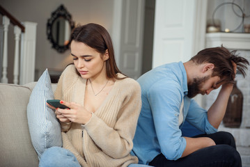 Obraz premium Modern couple at home. Man and woman concentrated on messaging with smartphones, ignoring each other and spending time on social media.